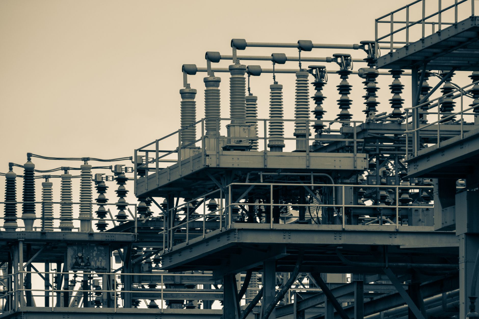 An aerial view of a rusted industrial plant next to a modern power substation, separated by a chain-link fence.