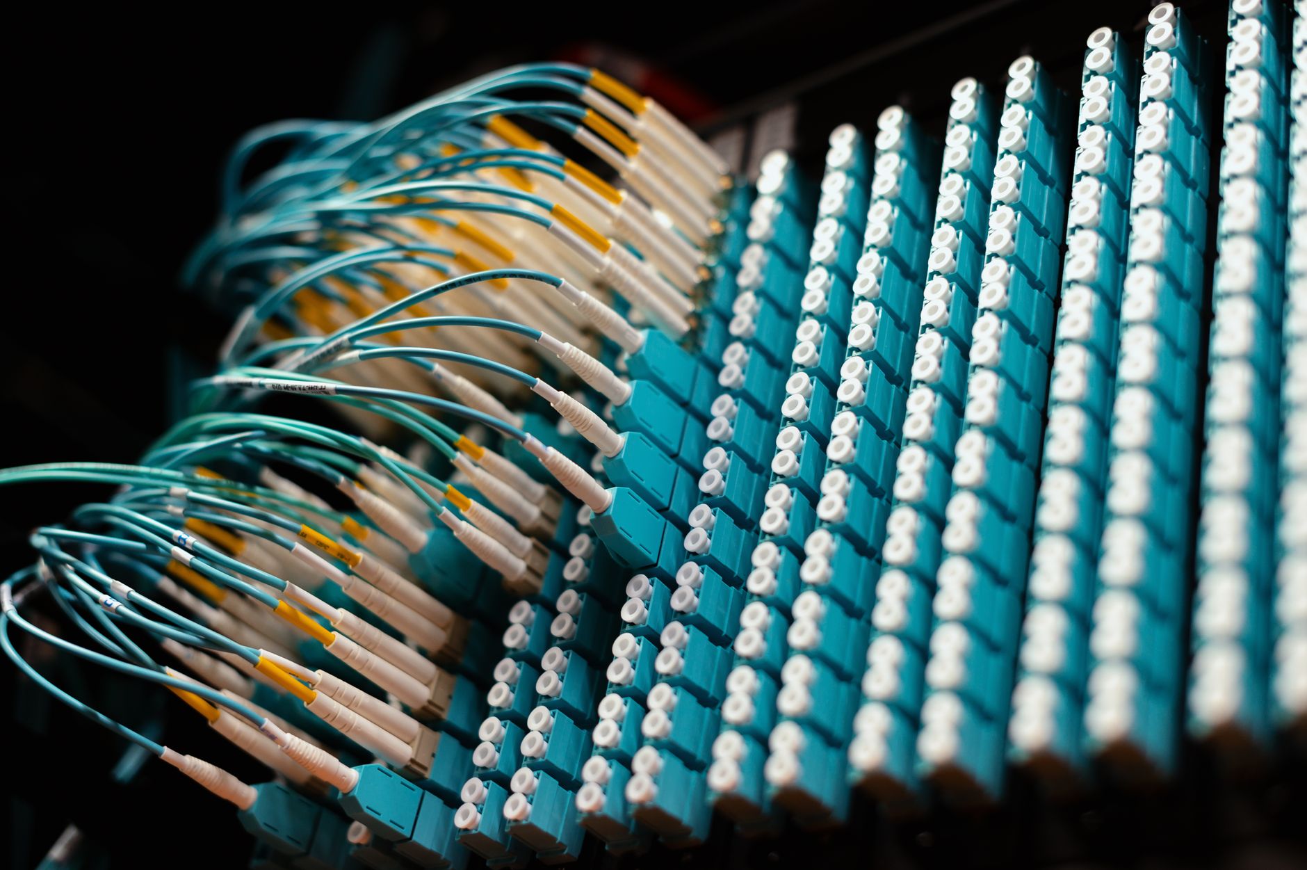 A glowing fiber optic cable intersecting with heavy industrial high-voltage electrical transmission lines against a dark sky