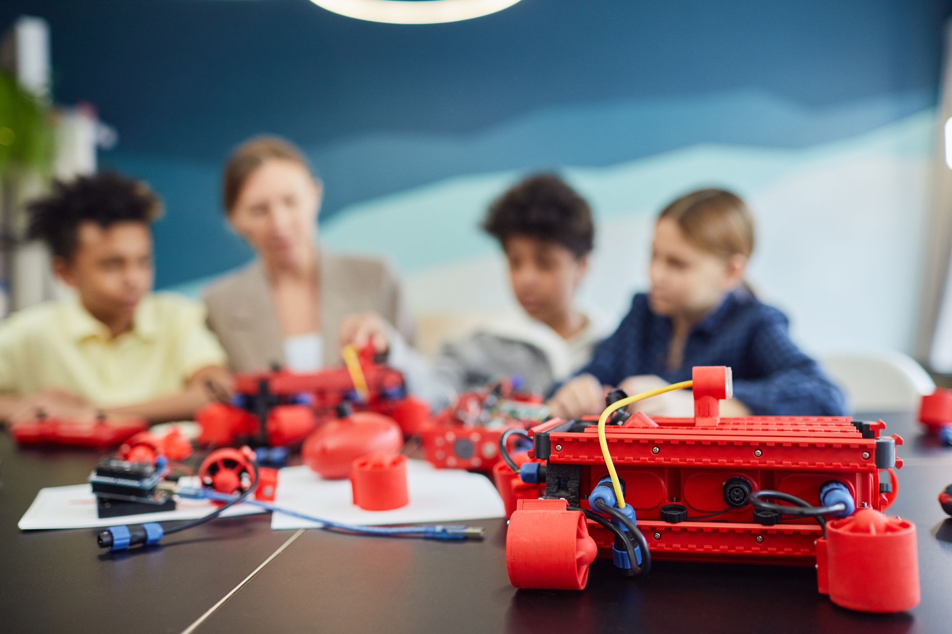 Students working on advanced industrial robotic arms in a brightly lit high school classroom, supervised by a corporate instructor.